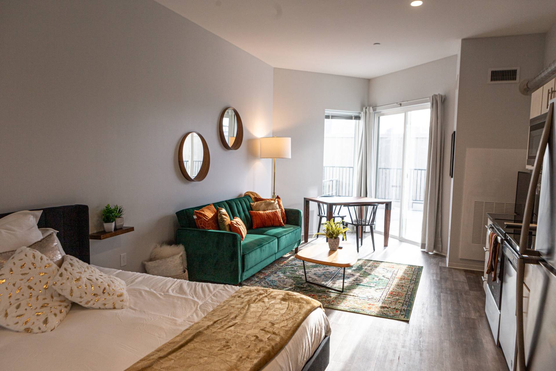 Studio apartment utilized as furnished guest suite. The bed is at the front of the image, looking towards a couch and sliding patio door. On the right is the kitchen area.